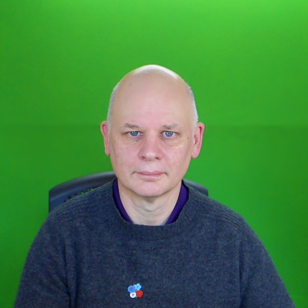 bald man sitting in a green room background wearing dark blue sweater