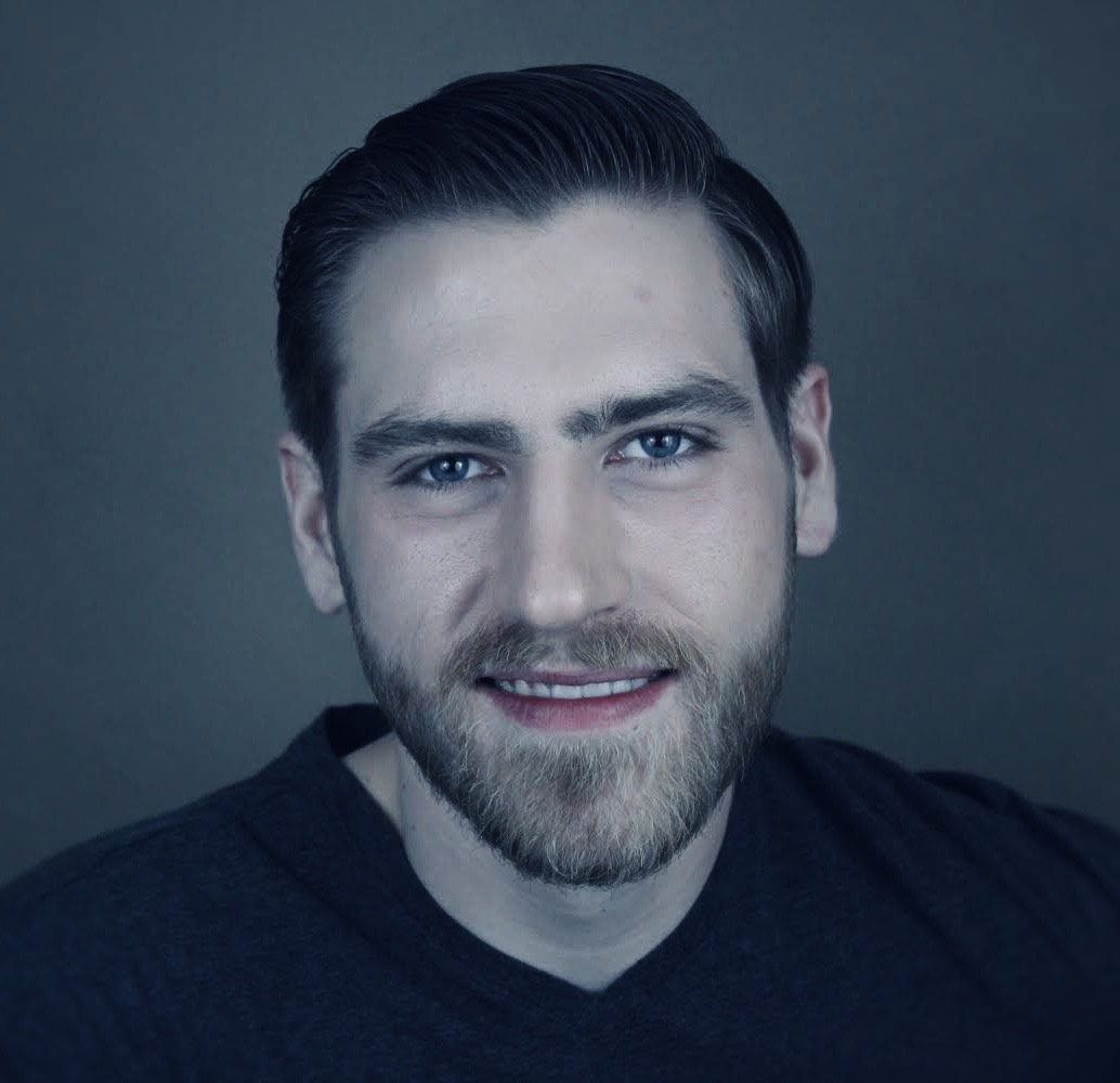 headshot of a smiling young man with beard wearing a black T-shirt